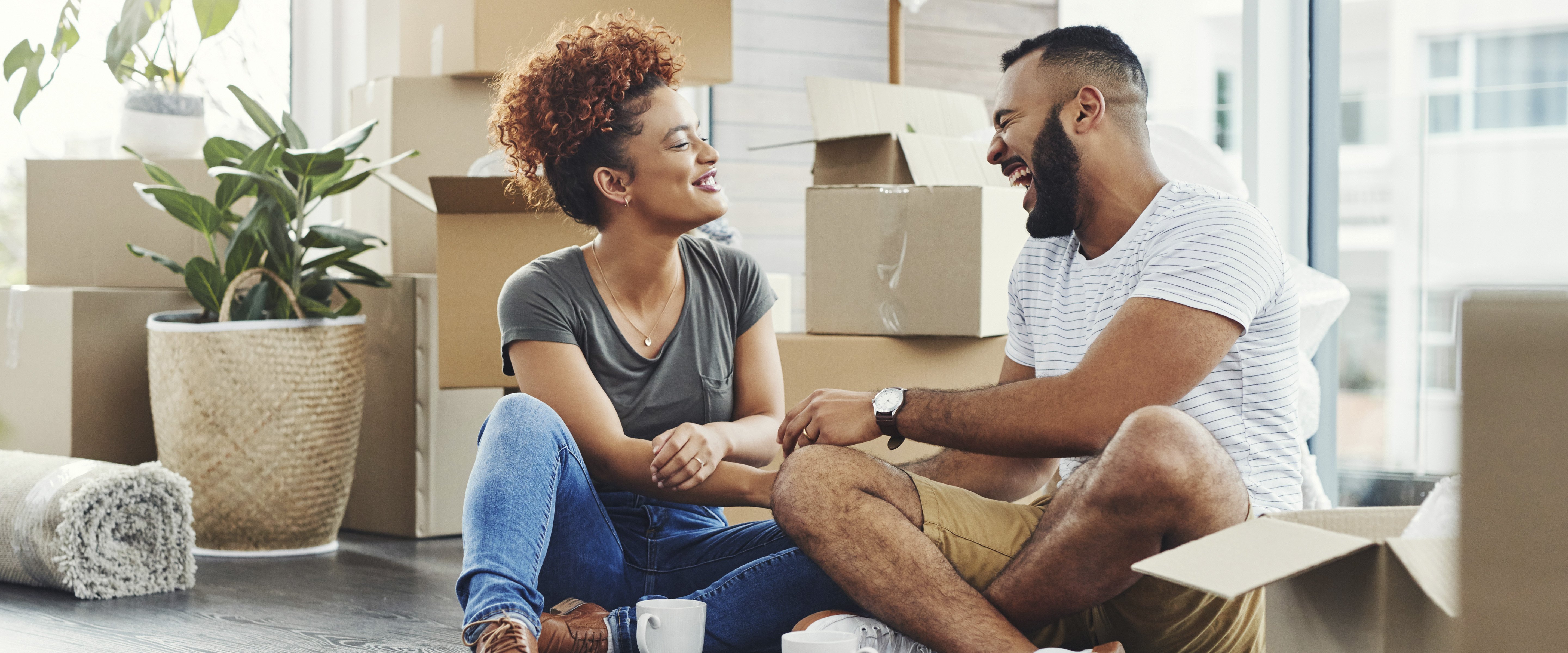 young couple sitting on floor of new home among moving boxes