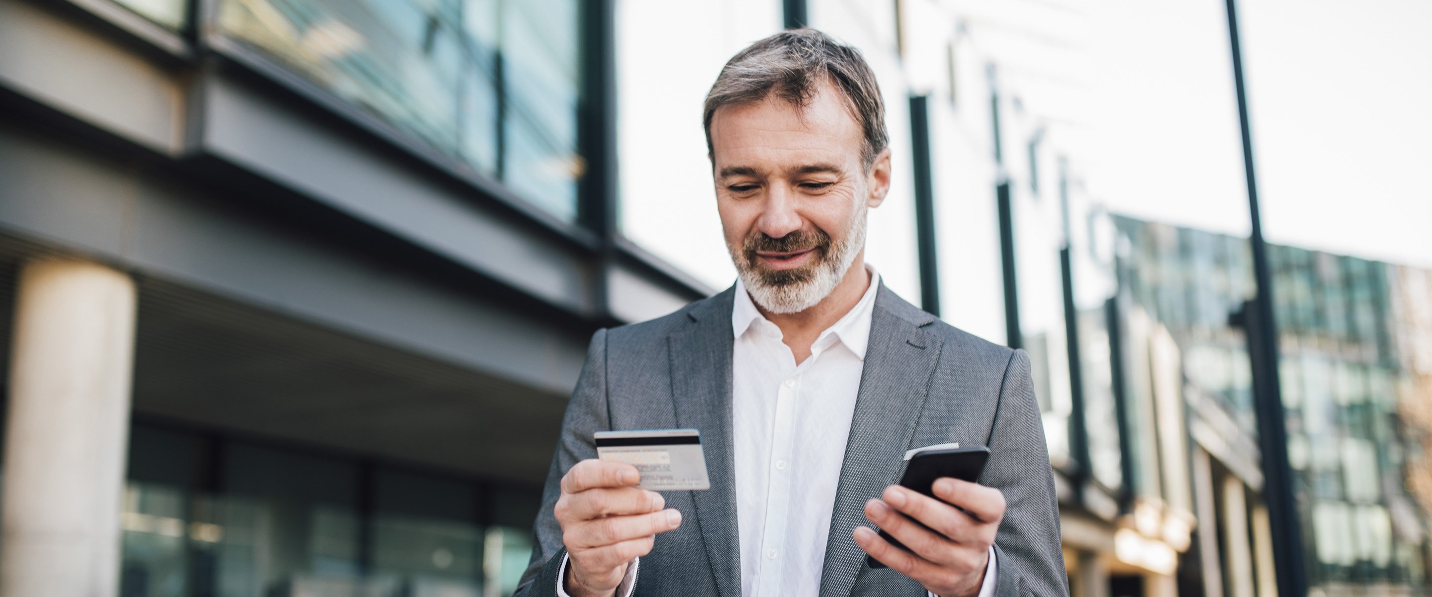 man outside office building using mobile phone and credit card